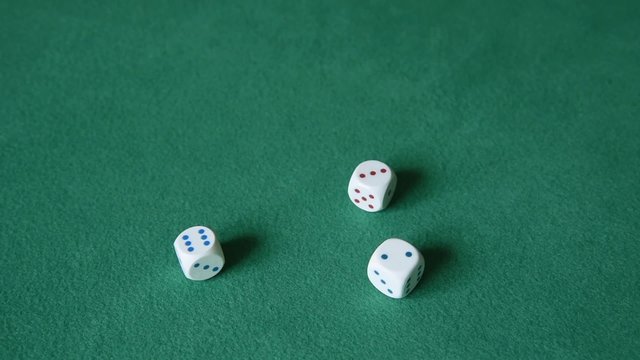 A hand of a man throwing three white dice on the green cloth. Slow motion.