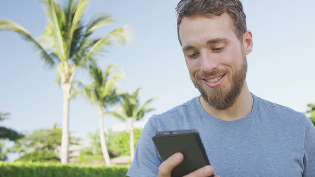 Smartphone man using mobile cell smart phone outdoors in summer. Handsome young casual man using mobile cell phone smiling happy. Urban male hipster. RED EPIC 90 FPS.