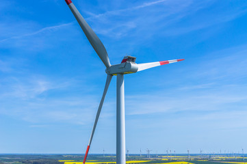 Luftbild und Nahaufnahme einer Windenergieanlage mit einem Windpark im Hintergrund und strahlend blauem Himmel