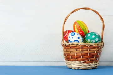 Easter eggs in beautiful and different colors lay  and in a wicker basket on blue wooden table