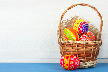 Easter eggs in beautiful and different colors lay on the fabric and in a wicker basket on blue wooden table