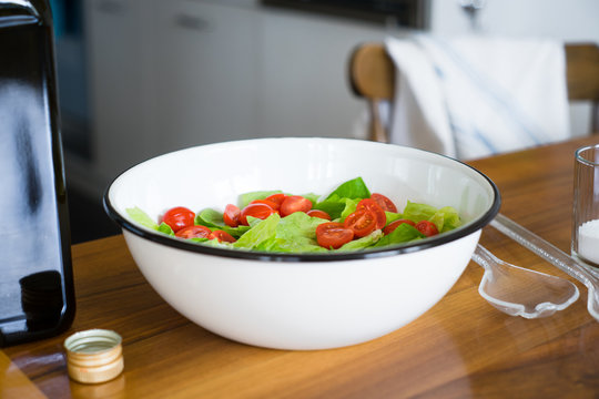 Green lettuce salad leaves and halfed cherry tomatoes in white enamel bowl. Selective focus.
