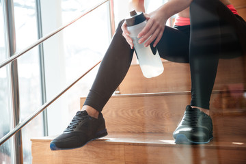 Legs of attractive woman athlete sitting on stairs in gym