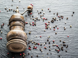 Colorful peppercorns and old pepper mill on the black background