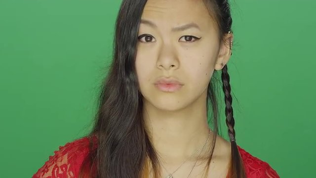 Young Asian woman staring and looking serious, on a green screen studio background