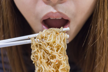 Noodle on chopsticks with people in background, shallow depth of
