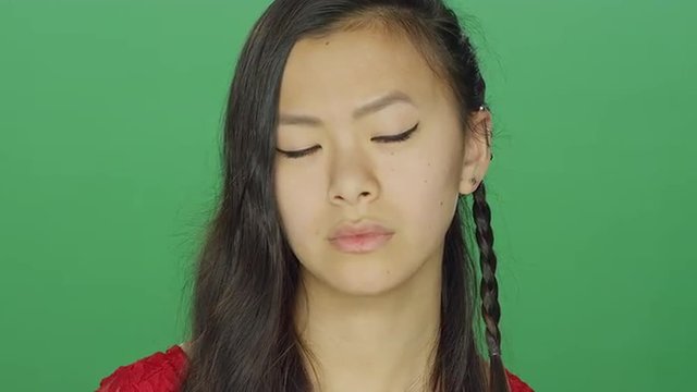 Young Asian woman staring and looking serious, on a green screen studio background