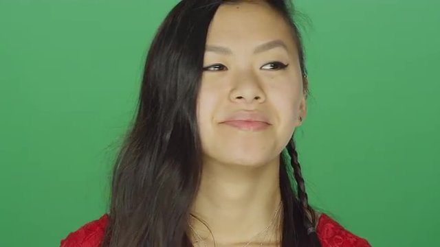Young Asian woman looking around and smiling, on a green screen studio background