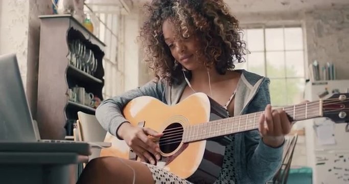 Attractive mixed race young girl learning to play guitar using laptop computer 