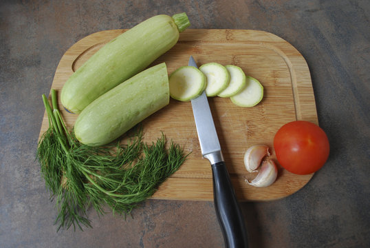 Vegetables (zucchini, tomato, garlic, parsley) with knife on a cutting board. Healthy eating. Preparation for cooking vegetable stew.