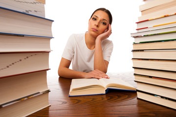 Sick and tired woman reading behind the table between two pile o