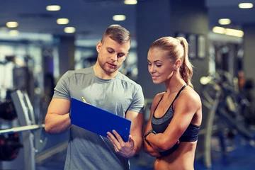 Tuinposter smiling young woman with personal trainer in gym © Syda Productions