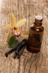 Vanilla pods, aromatherapy oil and orchid flowers on wooden back