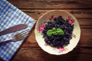 Sapling still in compost on a dinner plate with cutlery and a napkin on a rough wooden table
