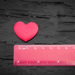 Red love heart being measured by a red ruler on a black wooden background