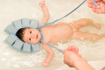 Baby girl swiming in the bath with special blue swiming mutch. Mother hands taking her head under water level
