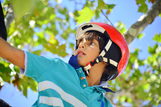 Bopy with red helmet climbing a tree
