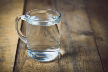 Glass of water on wood background. Toned photo.