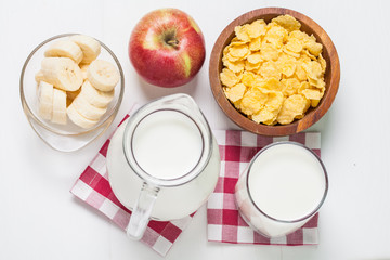 cornflakes with banana, apple and jar and glass milk on wooden table with textile napkin