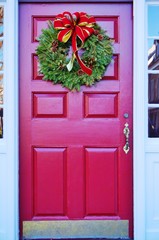 Christmas holiday pine wreath with a red bow on a red door