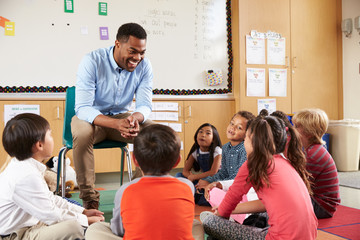 Elementary school kids sitting around teacher in a classroom