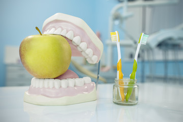 Composition. Denture, apple and toothbrushes in glass in dental surgery