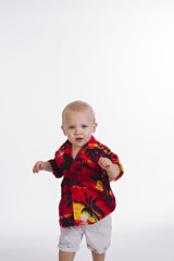 A young blonde male toddler dancing in a colorful shirt and shorts.