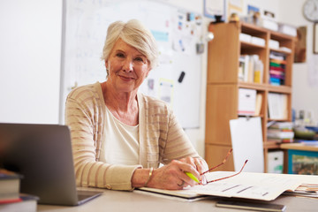 Portrait of senior female teacher working at her desk - Powered by Adobe