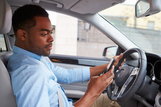 Young African American male driver using phone, in car view