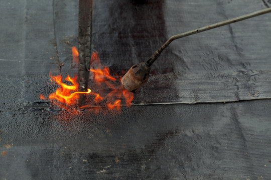 waterproofing roll bituminous material in the trench. construction worker manufacturer uses a gas burner propane tank fire.