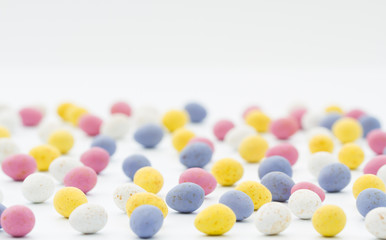 Colourful candy and chocolate Easter eggs scattered over a white background with copy space.