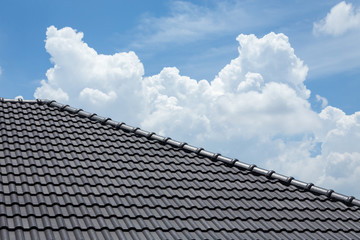 black tile roof of house with blue sky and cloud background