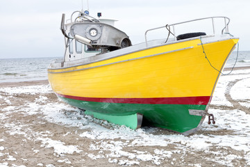 Naklejka premium Old yellow fishing boat on sea shore, on frozen, sandy beach with snow