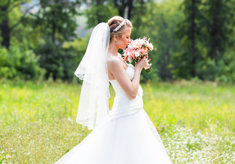 Beautiful bride with wedding bouquet of flowers outdoors in green park. © satura_