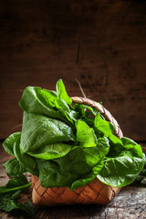 Fresh organic spinach in a wicker basket on an old wooden backgr