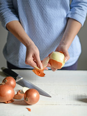 Woman hand peel fresh onion on white table
