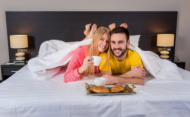 Happy young couple having breakfast tray on bed at home