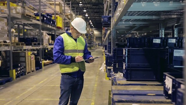 Worker on warehouse going along racks and checking containers on shelves