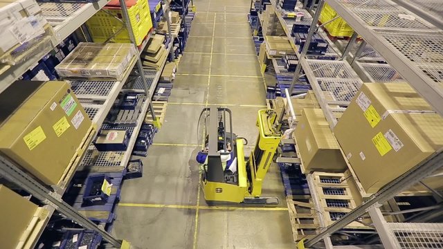 Storage worker on autoloader taking box from shelf and transporting. From above