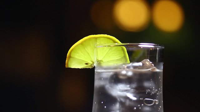 Color footage of a glass of soda with ice cubes and a hand putting a lemon slice in it.