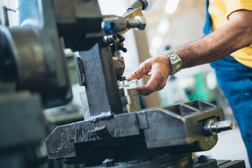 Close up photo of dirty workers hand doing some job on big metalworking machine. Selective focus.