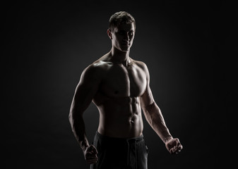 Sexy shirtless bodybuilder posing, looking at camera on black background.