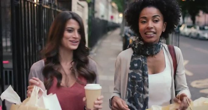 Two beautiful woman friends shopping walking through city 