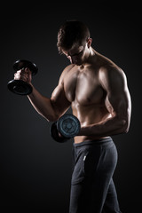 Fototapeta na wymiar Athletic man showing muscular body and doing exercises with dumbbells