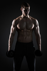 Muscular man showing perfect body with dumbbells on black background