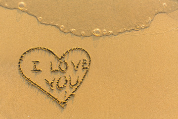 Heart that says I Love You - drawn on beach sand with a soft rolling wave.