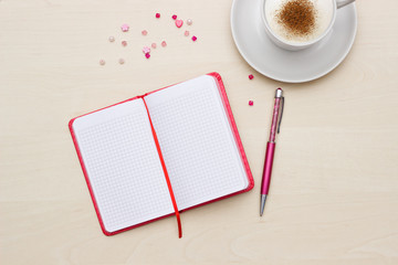 Red notebook with pen and coffee on wooden