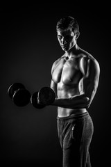 Handsome man showing perfect body with dumbbells on black backgr