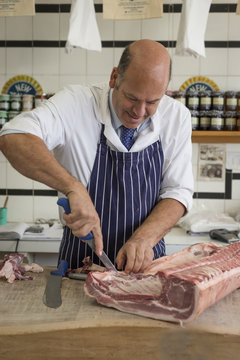 Butcher carving a rack of meat with a sharp knife