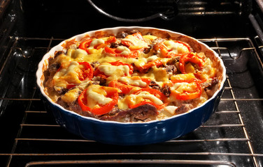 Potato with meat, tomato and cheese is baked in the oven. 